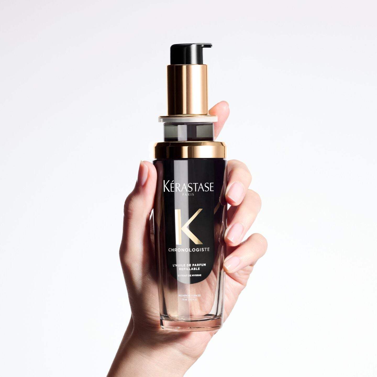 Chronologiste Huile De Parfum bottle in hand, elegant hair fragrance with rose, light wood, and musk notes for nourished, shiny hair.